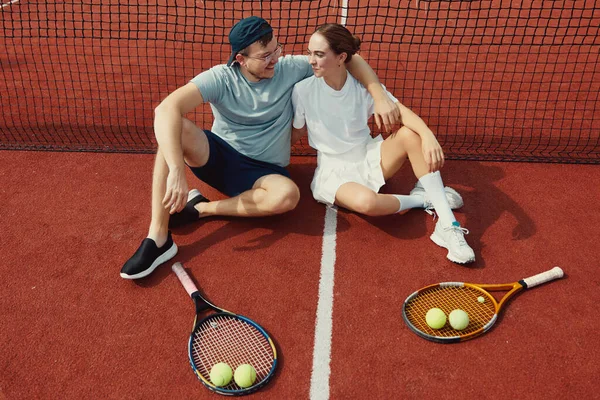 stock image Top view of happy couple sitting on the tennis court floor with rackets and balls. Friends are happy after a beautiful and fun match. Weekend and sunday activity for recreation