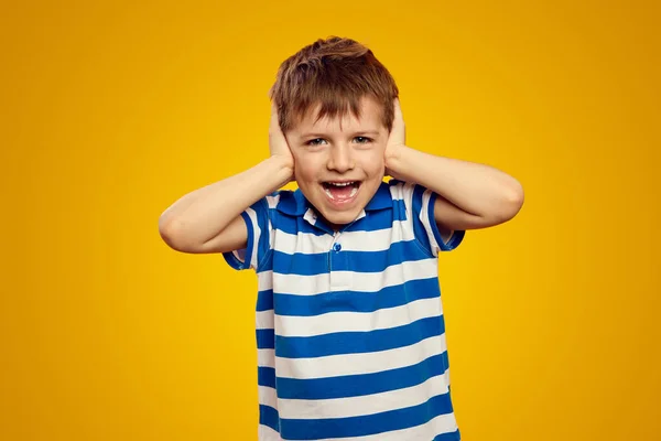 stock image Surprised little boy covering his ears with both hands not listening or overhearing, screaming with open mouth over yellow background