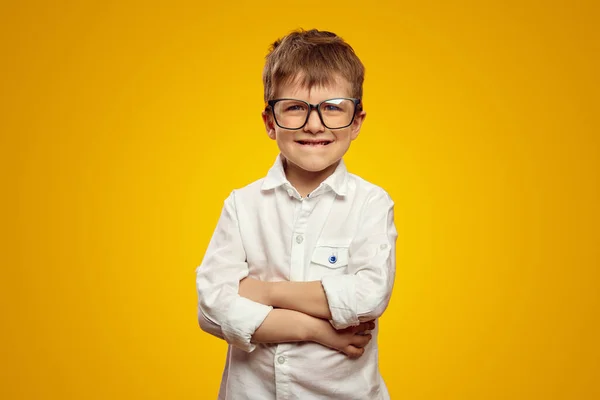 stock image Adorable kid wearing white shirt and eyeglasses standing with arms crossed while biting lips, isolated over yellow background and looking at camera