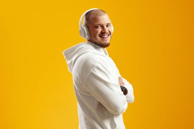 Beyaz kapüşonlu neşeli çekici erkek, gülümsüyor ve sarı arka planda el ele tutuşurken kulaklıkla en sevdiği şarkıyı dinliyor.