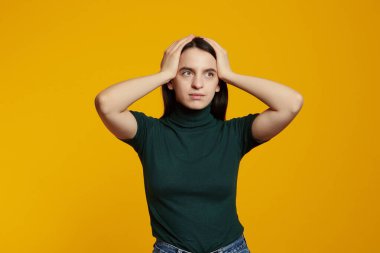 Sorunlu kızın el ele tutuşup paniklediği, tedirgin olduğu ve sarı arka plana şok olduğu bir fotoğraf.