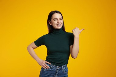 Gülümseyen neşeli kadın fotokopi çekilen yeri işaret ediyor ve sarı arka planda duran sevimli ve dostane bir ifadeyle kameraya bakıyor. Reklam kavramı.