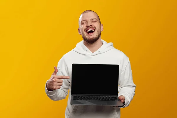 후드를 웃으며 노란색 컴퓨터를 손가락으로 가리키는 수염을 — 스톡 사진