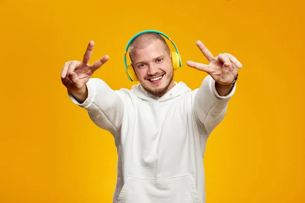 Przystojny Facet Białej Bluzie Słuchający Muzyki Żółtych Słuchawkach Pokazujący Gest — Zdjęcie stockowe