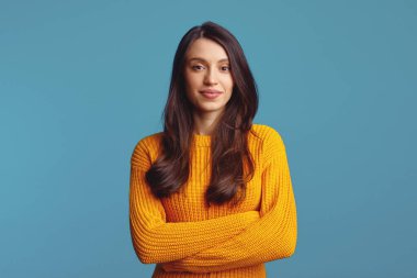 Normal turuncu kazak giymiş tatmin olmuş bir kadın modelin portresi doğrudan kameraya bakıyor, gülümsüyor ve mavi arka planda el ele tutuşuyor.