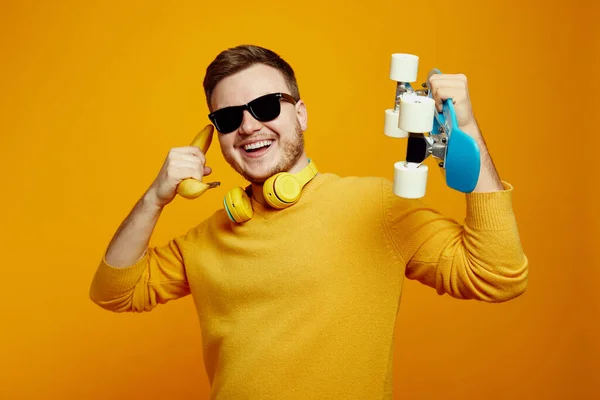Zabawny Człowiek Żółtym Swetrze Okularach Przeciwsłonecznych Trzymający Ręku Longboard Trzymający — Zdjęcie stockowe