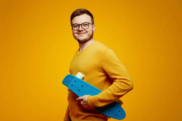 Szczęśliwy Młody Mężczyzna Żółtym Swetrze Okularach Trzyma Niebieską Longboard Ramieniu — Zdjęcie stockowe