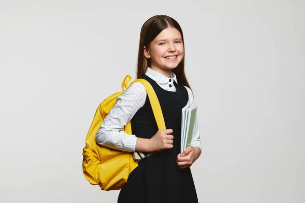 无忧无虑的女生 背着黄色的背包 在白底的学习过程中微笑着拥抱笔记本 回到学校的概念 — 图库照片