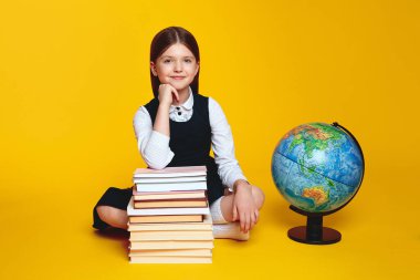 Dünya küresinin yanında, sarı arka planda izole bir şekilde otururken bir sürü kitabın elini tutan zeki kız öğrenci. Okul konseptine dönelim.