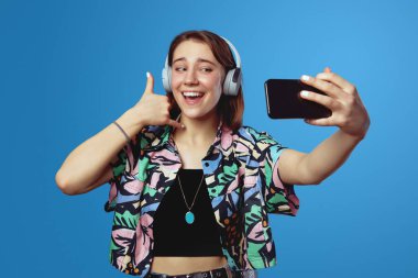 Genç gülümseyen esmer şık bir gömlek giyiyor, konuşan telefon gibi el ele tutuşuyor ve mavi arka planda izole edilmiş bir video görüşmesi yapıyor..