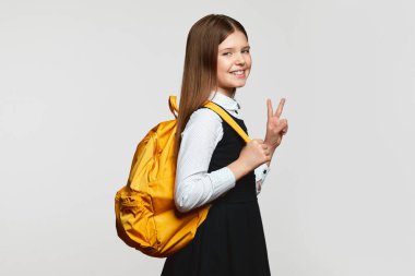 Sırt çantalı, kameraya gülümseyen ve beyaz arka planda tek başına dururken V işareti yapan heyecanlı bir kız öğrenci. Okul konseptine dönelim.