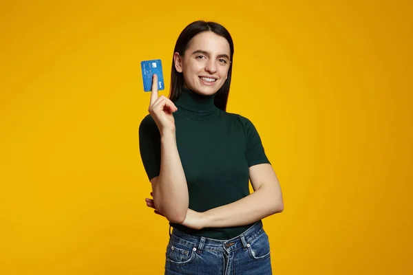 stock image Young smiling happy fun caucasian woman wearing green shirt, hold in hand mock up of credit bank card isolated on plain yellow background