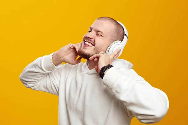 Gözleri kapalı neşeli genç bir adam sarı arka planda dans ederken kulaklıkla favori şarkıyı dinliyor ve gülümsüyor.