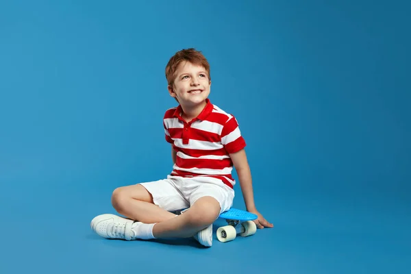 줄무늬 셔츠에서 즐거운 미소와 공간으로 파란색 배경에 스케이트 보드에 스톡 사진