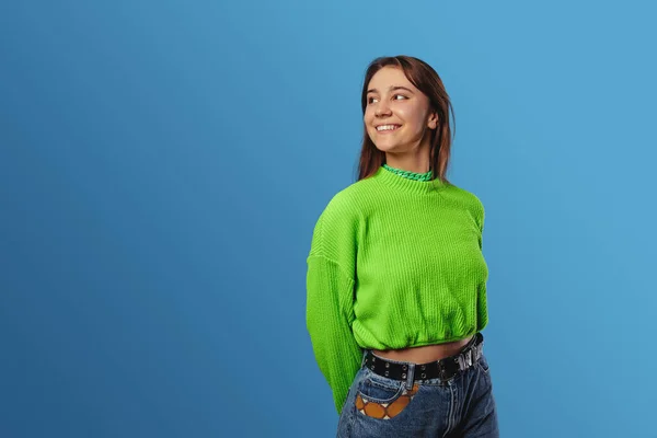 穿着绿色毛衣 面带微笑 站在蓝色背景下看着复印空间的快乐的年轻女士 — 图库照片