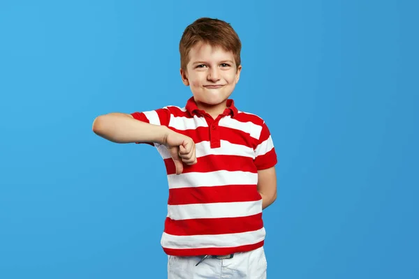 気に入らない 不満の肖像画 赤いストライプのシャツの小さな男の子は ジェスチャーの下に親指を示し 青い背景に隔離された不満を見ている — ストック写真