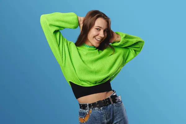 年轻而快乐的女模特 身穿绿色毛衣 手牵着手 微笑着看着相机 站在蓝色的背景下 — 图库照片