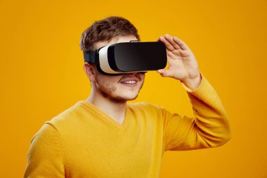 Modern VR kulaklıklı heyecanlı sakallı adam sarı arka planda izole edilmiş başka bir dünyayı yaşıyor.