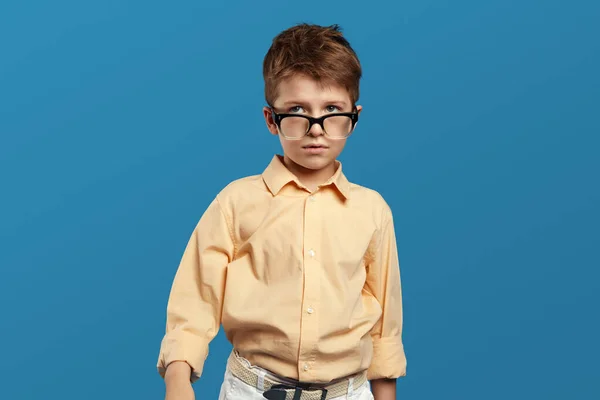 身穿米黄色衬衫 头戴眼镜 身穿米黄色衬衫 孤零零地站在蓝色背景下的有思想的十几岁的小男孩 — 图库照片