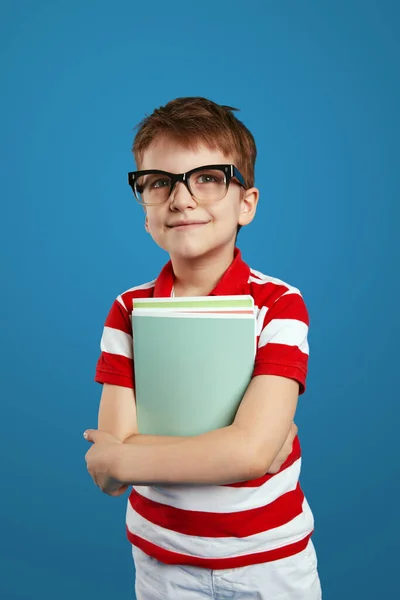 İnek gözlüklü zeki öğrenci, gülümseyip ders kitaplarını tutarken mavi arka planda tek başına duruyor. Okul konseptine dönelim..