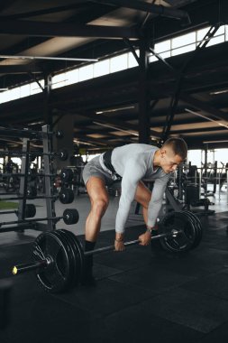 Modern spor salonunda halter kaldıran bir adamın dikey fotoğrafı. Kapalı alanda yatay çekim. Güç eğitimi, disiplin ve iş başındaki yaşam tarzı.