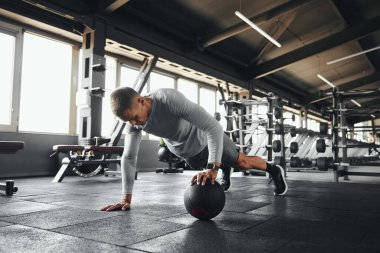 Modern spor salonunda spor yaparken kaslı bir adam tek eliyle spor yapıyor.