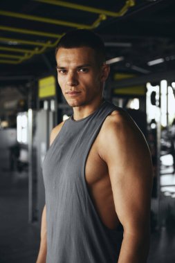 Spor salonunda antrenman yaptıktan sonra yakışıklı beyaz erkek sporcunun dikey yakın çekimi. Spor kıyafetleri giymiş, kameraya poz veren ciddi bir fitness eğitmeni..