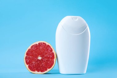 Beyaz bir kozmetik şişesi canlı kırmızı bir greyfurt dilimi ile temiz mavi bir arkaplan ile eşleştirilir, tazelik, sağlık ve güzellik paketini sembolize eder..