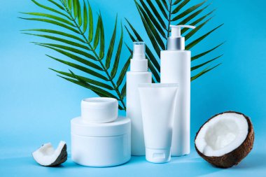 Cilt bakımındaki doğal güzelliği ve tazeliği sembolize eden canlı mavi bir arka planda yeşillik ve hindistan cevizi yarısıyla tamamlanmış beyaz tenli şişeler ve kavanozlardan oluşan şık bir kompozisyon.