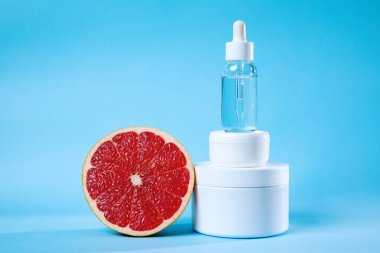 Beyaz bir kavanoz, serum şişesi ve yarım greyfurt içeren doğal cilt ürünlerini gösteren bir resim, doğal güzelliği ve tazeliği sembolize ediyor..