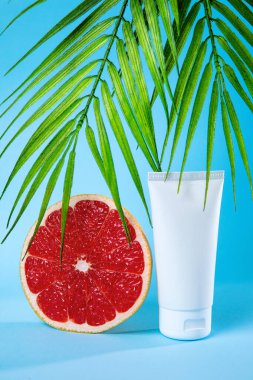Taze bir greyfurt, tropikal palmiye yaprakları ve parlak mavi bir arka planda doğal güzelliği ve tazeliği simgeleyen bir cilt tüpü içeren canlı bir kompozisyon..