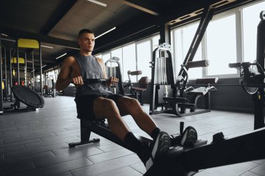 Spor salonunda kürek çekme makinesinde pratik yapan yakışıklı bir erkek. Spor salonundaki kürek çekme makinesinde çalışan atletik genç adam. Ağırlık azaltma ve kardiyovasküler egzersiz kavramı.