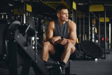 Sağlam vücutlu yorgun bir adam spor salonunda kürek çektikten sonra biraz soluklanıyor. Kararlı ifadesi kendini adadığını ve sıkı çalıştığını gösteriyor.