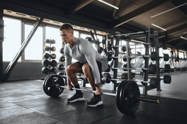 İlaç topları ve eğitim teçhizatlarıyla çevrili, parlak, düzenli bir spor salonunda halter kaldıran bir adam, güç, kontrol ve spor yapmaya bağlılığını gösterir.
