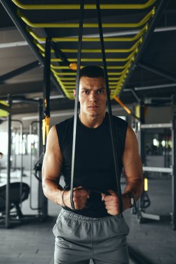 Spor giyim sektöründeki yakışıklı atletik adam spor salonunda egzersiz yapmak için bir direniş bandından yararlanıp kendini adamışlığını ve fiziğini ön plana çıkarıyor..