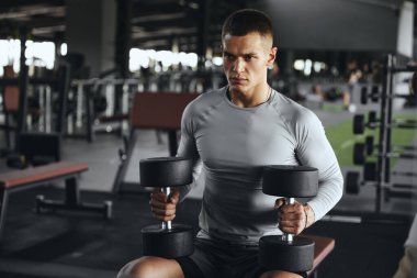 Spor bankında dambılla egzersiz yapan güçlü odaklı bir adam. Güç eğitimi, disiplin ve iş başındaki yaşam tarzı.