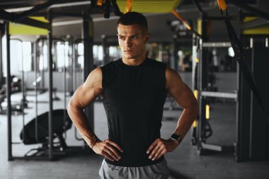 Spor salonundan sonra ciddi bir fitness sporcusu. Spor elbiseli yakışıklı bir fitness hocasının yatay fotoğrafı. Kameraya kalçalarını dayayıp poz veriyor..