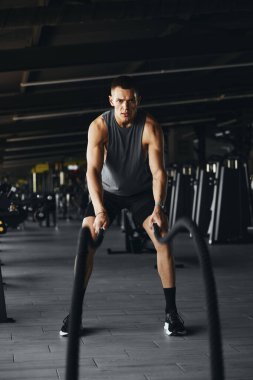 İyi donanımlı bir spor salonunda ağır savaş halatları ile tam boy atletizm eğitiminin dikey fotoğrafı dayanıklılık ve dayanıklılık gösteriyor. Sporcu erkek spor salonunda halatla çalışıyor.