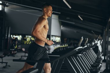 Spor salonunda koşu bandında koşan üstsüz sporcunun yan görünüşü. Sportif erkek, spor kulübünde sağlık ve zindelik üzerine çalışıyor. Spor çalıştırma konsepti.
