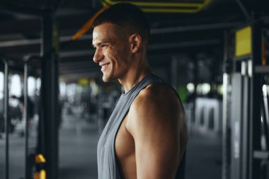 Spor salonundan sonra neşeli bir sporcunun yan görünüm portresi. Spor kıyafetleriyle yakışıklı bir fitness hocasının yatay fotoğrafı. Kameraya poz verirken gülümsüyor..