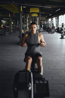 Modern spor salonunda çalışan ve kablo çekme makinesi kullanan güçlü, genç ve formda bir erkeğin dikey foto görüntüsü. Spor salonunda kürek çeken yakışıklı bir sporcu..
