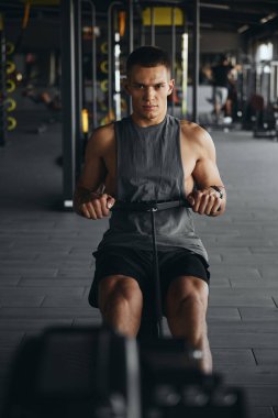 Modern bir spor salonunda kürek çeken formda bir adamın dikey fotoğrafı. Spor salonunda antrenman yapan atletik genç adam, kilo kaybı ve kardiyo üzerine odaklanıyor..