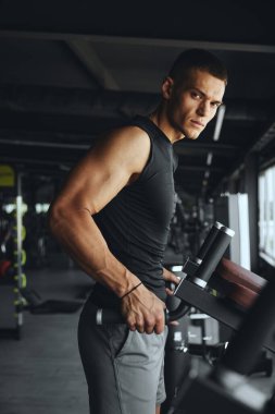 Yakışıklı vücut geliştiricinin dikey fotoğrafı kendini paralel çubuklarda yoğun ve zorlu bir idmana hazırlar ve maksimum sonuçları hedefler.