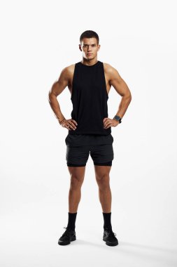 Atletik bir genç, siyah spor kıyafeti giyerek beyaz bir arka plana karşı dayanıklılık ve zindelik betimliyor..