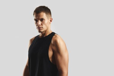 Kolsuz, siyah bluzlu genç adam sade bir arka plana karşı güvenle poz veriyor. Güçlü ve kararlı ifadesi uygunluğu ve bağlılığı vurguluyor..