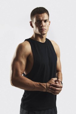 Kameraya bakan kaslı adamın dikey fotoğrafı. Beyaz arka planda siyah kolsuz gömlek giyiyor. Güç, zindelik ve kararlılık göstergesi. Vücut geliştirme, fitness ve sağlık hizmeti kavramı