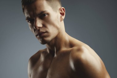 Yakışıklı, kaslı bir gencin gri arka planda kendine güvenen bir portresi. Moda reklamcılığı veya fitness markası için ideal..