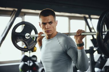 Fitness merkezinde halterle egzersiz yapan güçlü bir erkek. Vücut geliştiren adam ağır sıkletlerle spor salonunda çalışıyor. Güç eğitimi, disiplin ve iş başındaki yaşam tarzı.