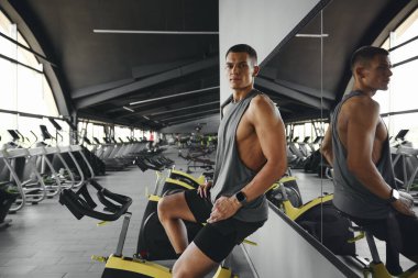 Spor kıyafetli yorgun adam spor salonunda spor bisikletle egzersiz yaptıktan sonra dinleniyor. Genç adam bisiklete bindikten sonra dinleniyor..