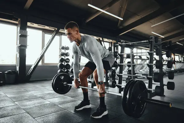 İyi donanımlı bir spor salonunda ağır bir halteri kaldıran kaslı bir adam. Deadlift ağırlık ve antrenman malzemeleriyle dolu modern bir alanda güç, odaklanma ve zindelik gösteriyor.